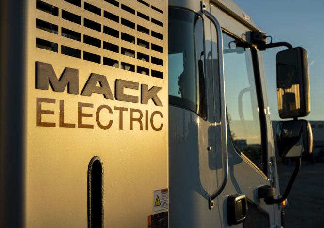Close-up of the side of a Mack Electric truck, with "MACK ELECTRIC" branding prominently displayed in the sunlight
